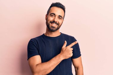 Gündelik giysiler giyen genç İspanyol adam gülümseyen, eli ve parmağı yana doğru gösteren. 