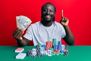 Elinde 100 dolarlık banknotlarla poker oynayan yakışıklı genç bir adam bir fikir veya soru işareti ile gülümsüyor. 
