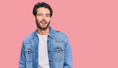 Gündelik kıyafetler giyen genç İspanyol adam kameraya seksi bir ifadeyle bakıyor, neşeli ve mutlu bir yüzle.. 