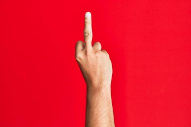 Arm of caucasian white young man over red isolated background showing provocative and rude gesture doing fuck you symbol with middle finger 