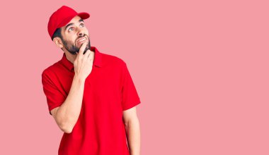 Sakallı, teslimat üniformalı genç yakışıklı bir adam bir soru hakkında endişeli ve gergin bir şekilde düşünüyor. 