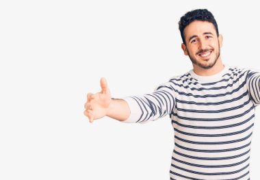 Gündelik giysiler giymiş genç İspanyol adam kameraya bakıp sarılmak için kollarını açmış gülümsüyor. Mutluluğu kucaklayan neşeli bir ifade.. 