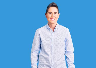 Kısa saçlı, iş kıyafetleri giyen, yüzünde mutlu ve havalı bir gülümseme olan genç bir kadın. şanslı kişi. 