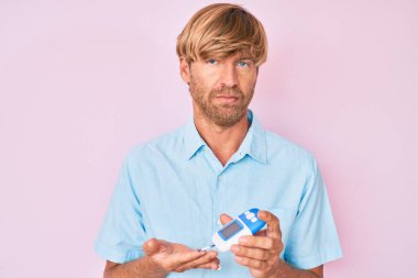 Glikoz ölçer kullanan genç sarışın adam yüzünde ciddi bir ifadeyle rahatlamış. Basit ve doğal bir şekilde kameraya bakıyorsun.. 