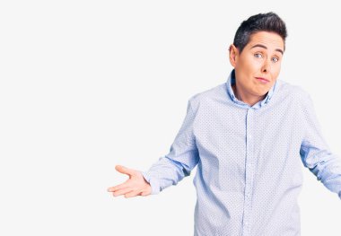 Kısa saçlı, iş kıyafetleri giyen, elleri ve kolları havada, kafası karışmış genç bir kadın. şüphe kavramı. 