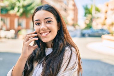 Genç İspanyol kadın gülümsüyor. Şehirdeki akıllı telefondan konuşuyor..