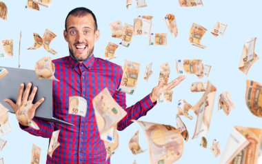 Bilgisayarda çalışan yakışıklı genç adam zaferi mutlu bir gülümsemeyle kutluyor ve kazanan elleri kaldırarak ifade ediyor.