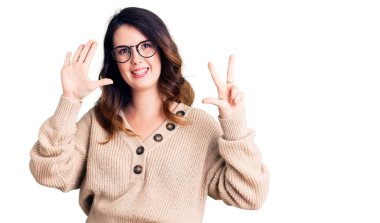 Güzel, genç, esmer bir kadın, günlük kıyafetler ve gözlük takıyor. Sekiz numaralı parmaklarıyla gösteriyor ve işaret ediyor. Kendinden emin ve mutlu gülümsüyor.. 