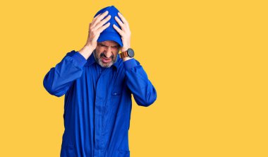 Orta yaşlı yakışıklı, tamirci üniforması giyen baş ağrısı çeken çaresiz ve stresli bir adam. Çünkü acı ve migren ağrısı var. Eller başının üstünde.. 