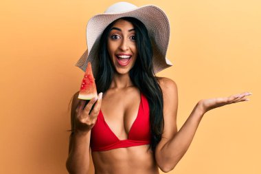 Güzel İspanyol kadın bikini giyip karpuz yiyor zaferi kutluyor mutlu bir gülümsemeyle ve ellerini kaldırarak kazanan bir ifadeyle. 