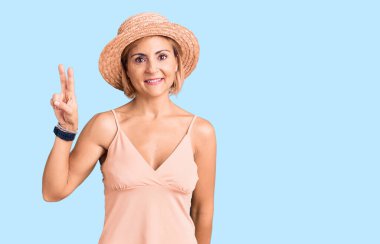 Yaz şapkası takan genç sarışın kadın kameraya bakıp zafer işareti yapıyor. İki numara.. 