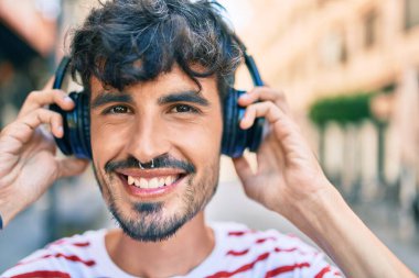 Mutlu gülümseyen ve kulaklık takan genç İspanyol adam şehrin caddesinde yürüyor..
