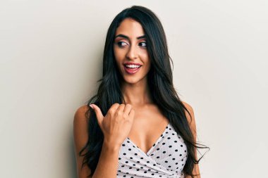 Güzel İspanyol kadın, günlük kıyafetler giyip gülümsüyor, gülümsüyor ve başparmağıyla yan tarafa bakıyor.. 