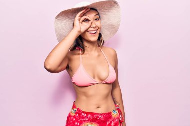 Bikini giyen ve şapka takan genç bir kadın el hareketleriyle gülümseyen, mutlu yüzüyle parmaklarından bakan bir jest yapıyor.. 