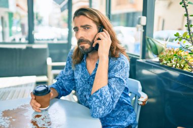 Orta Doğulu, üzgün yüzlü, akıllı telefonla konuşan ve kahve içen genç bir adam..