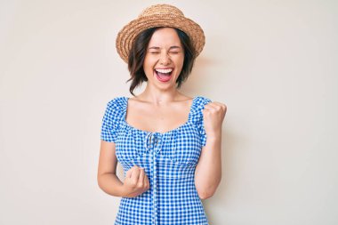 Yaz şapkası takan genç ve güzel bir kız şaşkınlık ve şaşkınlık içinde kollarını kaldırarak ve gözlerini kapayarak başarıyı kutluyor. 