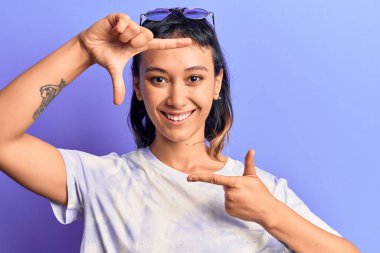 Gündelik kıyafetler giyen, gülümseyen, elleri ve parmakları gülen yüzlü genç bir kadın. yaratıcılık ve fotoğrafçılık kavramı. 