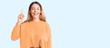 Gündelik giysiler giymiş güzel genç bir kadın başarılı bir fikirle işaret ediyor. Heyecanlı ve mutlu. Bir numara.. 