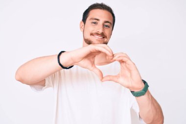 Gündelik beyaz tişört giyen, aşık gülümseyen ve elleriyle kalp sembolü yapan genç yakışıklı bir adam. romantik kavram. 