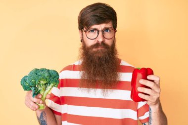 Uzun sakallı, elinde brokoli, kırmızı biber kuşkusu olan, sinirli ve sorunlu genç, yakışıklı bir adam. negatif kişi. 