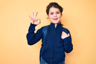 Sevimli İspanyol çocuk sırt çantasını tutuyor. Parmaklarıyla imza atıyor, gülümsüyor. Mükemmel bir sembol. 