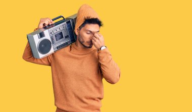 Yakışıklı Latin Amerikalı genç adam müzik kutusu tutuyor, müzik dinliyor burnu ve gözleri ovuşturup yorgun ve başı ağrıyor. Stres ve hüsran kavramı. 