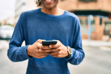 Genç Afrikalı Amerikalı adam şehrin caddesinde akıllı telefon kullanarak mutlu gülümsüyor..