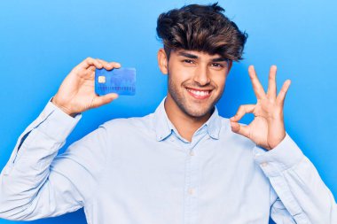 Genç İspanyol adam kredi kartı tutuyor. Parmaklarıyla imza atıyor, gülümsüyor. Mükemmel bir sembol. 