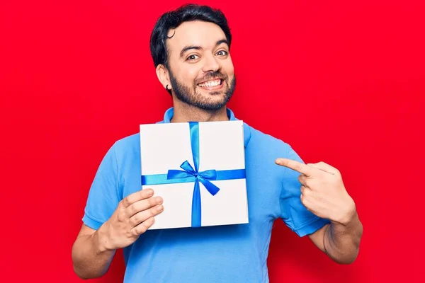 Jovem Hispânico Homem Segurando Presente Sorrindo Feliz Apontando Com Mão — Fotografia de Stock