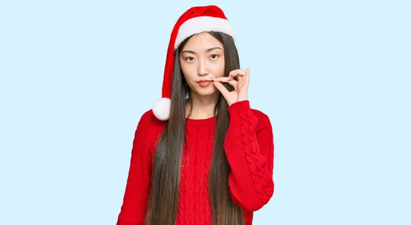 クリスマスの帽子の口と唇を身に着けている若い中国の女性は指でZipとしてシャットダウンします 秘密裏に黙ってタブーを語る — ストック写真