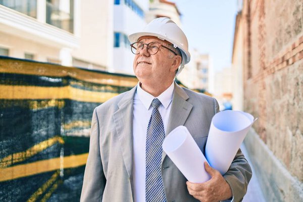 Senior grey-haired architect man holding blueprints walking at street of city
