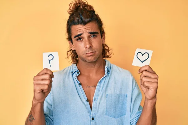 Jovem Hispânico Segurando Coração Ponto Interrogação Lembrete Expressão Indolor Confuso — Fotografia de Stock