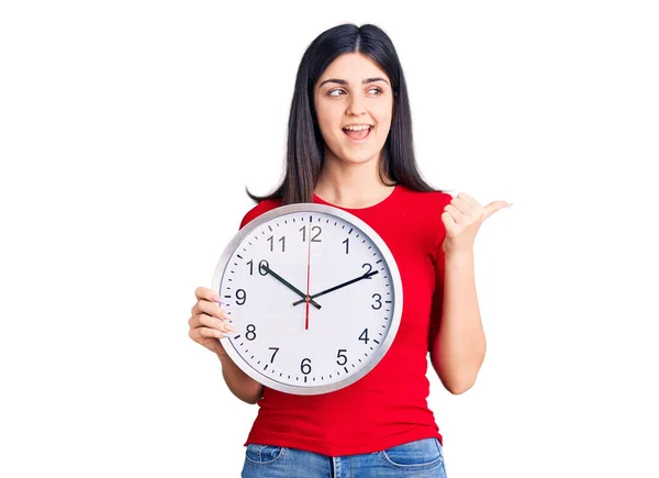 Young Beautiful Girl Holding Clock Pointing Thumb Side Smiling Happy — ストック写真