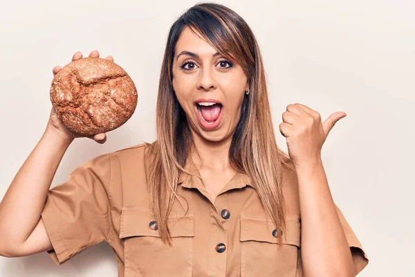 Jovem Bela Mulher Segurando Pão Apontando Polegar Até Lado Sorrindo — Fotografia de Stock