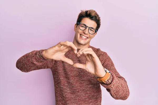 カジュアルなセーターを着たハンサムな白人男性と 手でハートのシンボルの形をする愛に微笑む眼鏡 ロマンチックなコンセプト — ストック写真