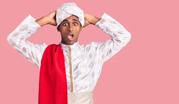 African handsome man wearing tradition sherwani saree clothes crazy and scared with hands on head, afraid and surprised of shock with open mouth