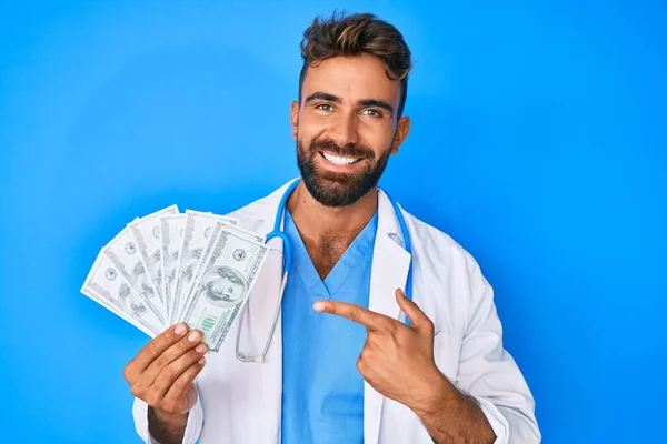 Joven Hispano Vistiendo Uniforme Médico Sosteniendo Dólares Sonriendo Feliz Señalando — Foto de Stock