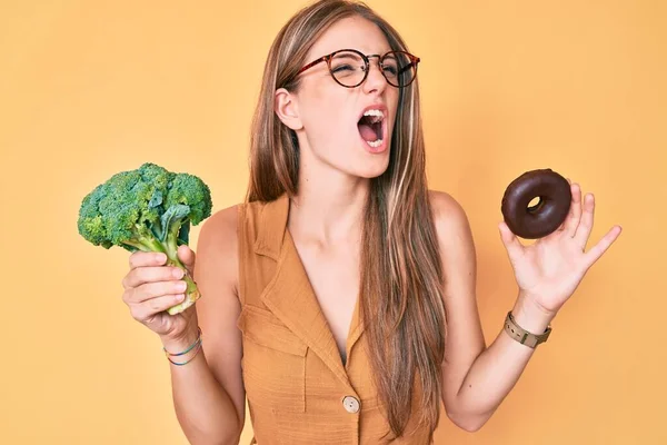 Young Blonde Girl Holding Broccoli Chocolate Donut Angry Mad Screaming — Stock Photo, Image