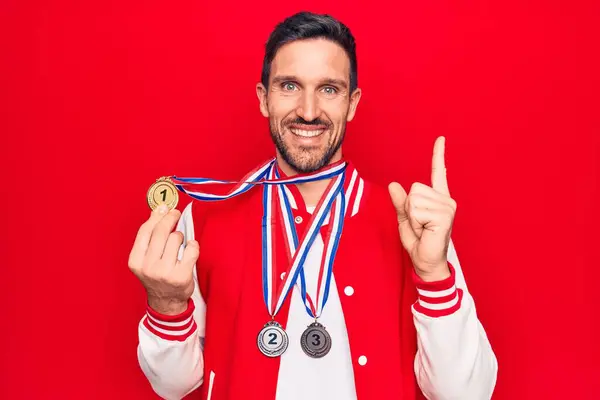 年轻英俊的运动员站在孤立的红色背景上 微笑着 手指手画脚地指向旁边 赢得奖牌 — 图库照片