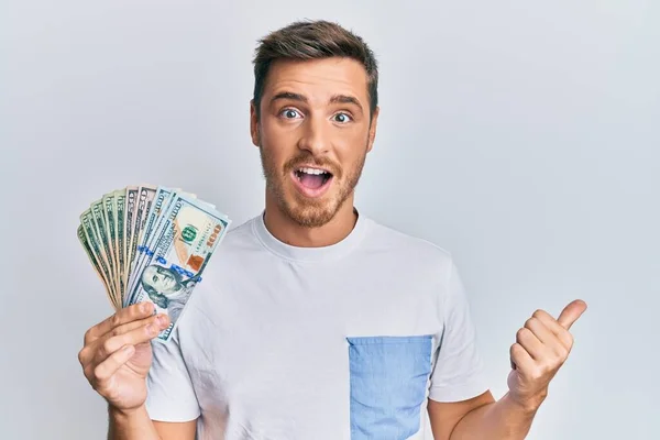 Hombre Caucásico Guapo Sosteniendo Dólares Apuntando Pulgar Hacia Lado Sonriendo —  Fotos de Stock