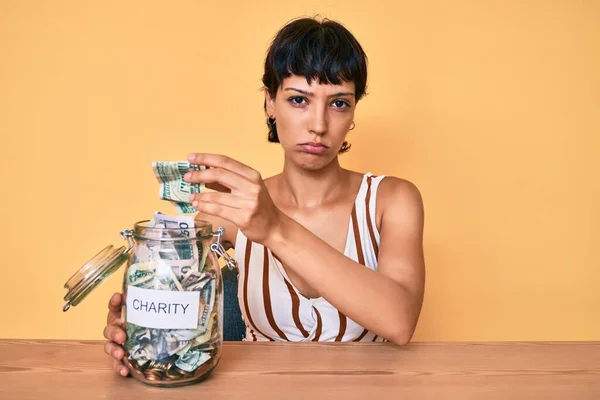 Beautiful brunettte woman holding charity jar with money depressed and worry for distress, crying angry and afraid. sad expression.