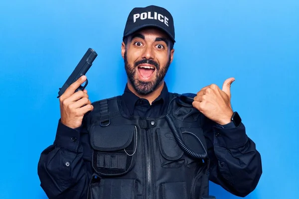 Młody Latynos Mundurze Policyjnym Trzymający Pistolet Skierowany Kciukiem Bok Uśmiechnięty — Zdjęcie stockowe