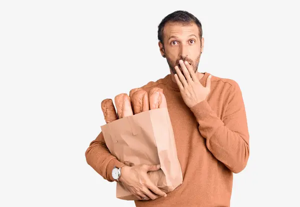 Junger Gutaussehender Mann Mit Papiertüte Und Brotdeckel Der Hand Schockiert — Stockfoto