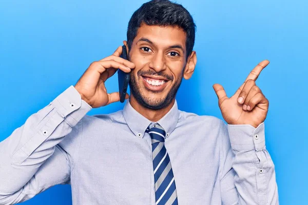 Genç latin adam akıllı telefonda konuşuyor gülümsüyor mutlu bir şekilde el ve parmak kenarı işaret ediyor. 