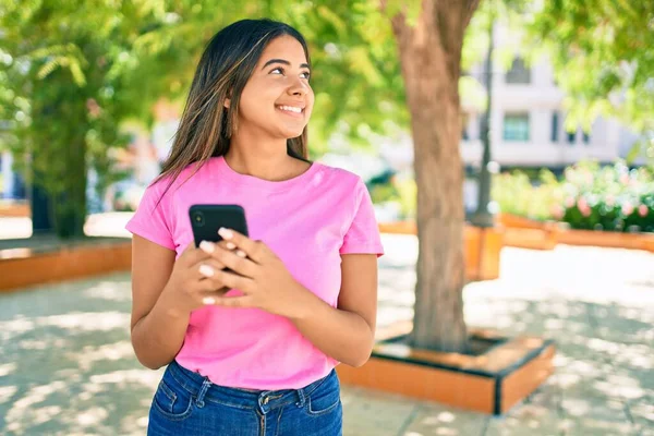 Young latin woman smiling happy using smartphone at the city.