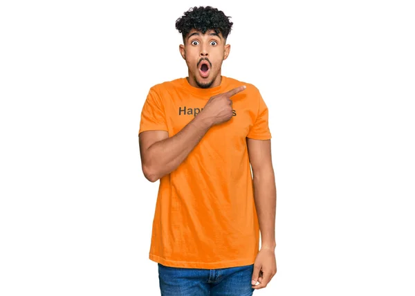 年轻的阿拉伯男子穿着印有快乐信息的T恤衫 手指指向旁边 张开嘴惊讶的表情 — 图库照片
