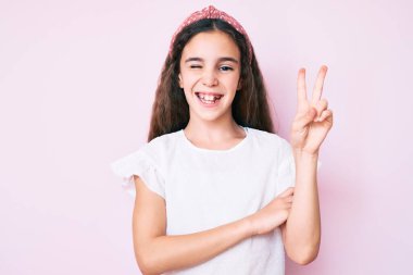 Gündelik kıyafetler giyen tatlı İspanyol kız çocuğu ve Diadem gülüyor kameraya göz kırparak zafer işareti yapıyor. İki numara.. 