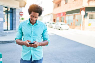 Genç, yakışıklı, Afro-Amerikan bir adam günlük giysiler giyip mutlu gülümsüyor. Yüzünde gülümsemeyle şehrin caddesinde akıllı telefon kullanarak dikiliyorsun..