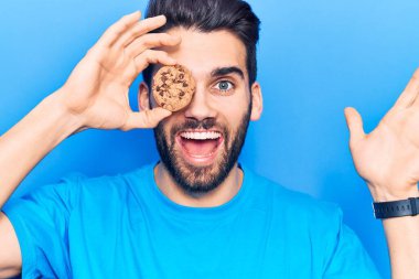 Sakallı, elinde çikolatalı kurabiyeyle genç yakışıklı adam başarıyı mutlu bir gülümsemeyle ve kazanan yüz ifadesiyle kutluyor. 