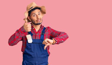 Yakışıklı Latin Amerikalı, tamirci üniforması giyen, baş parmak kaldıran, anlaşmazlık ve uzlaşma ifadesi takınan genç adam. çılgın çatışma 